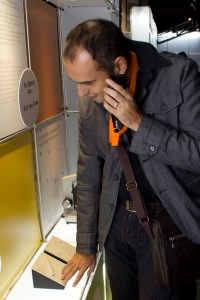 Photograph of a man listening to an audio device while touching a tactile exhibit